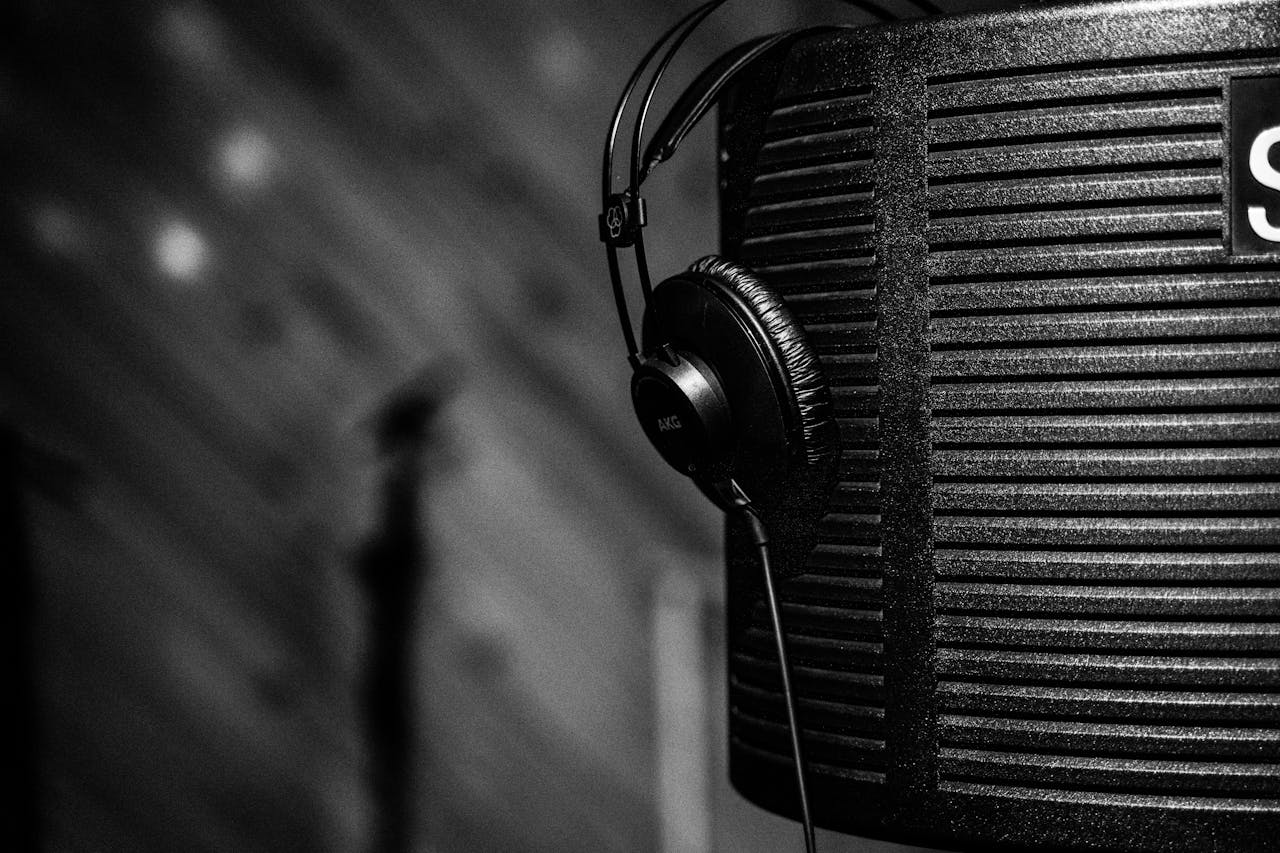 Close-up grayscale image of studio headphones hung on acoustic panel, depicting a professional music production environment.